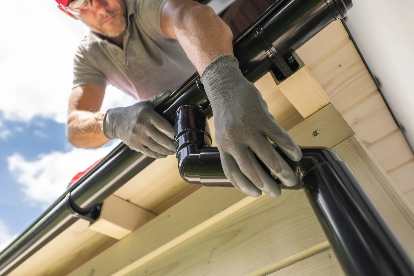 A roof plumber fitting a new black downpipe to a home's guttering